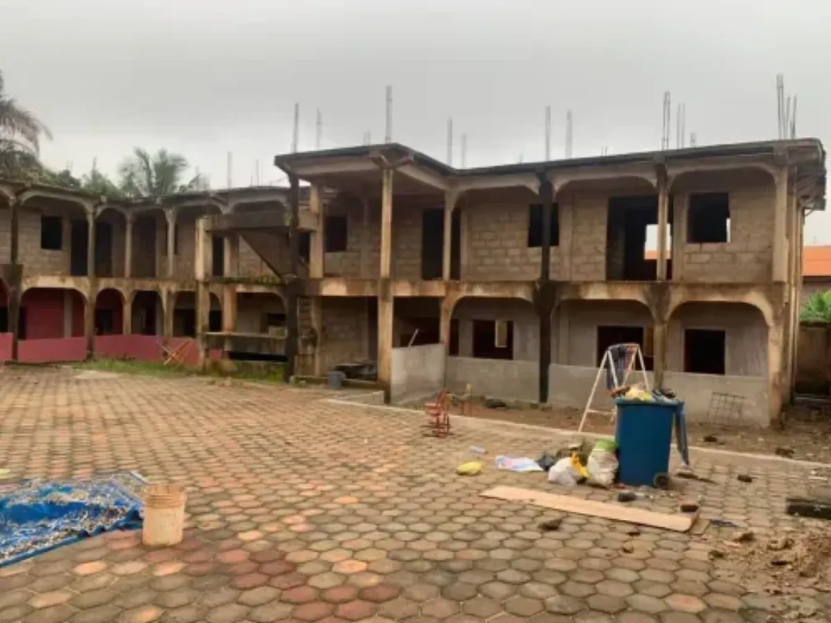 Het casco van de school in Daban vanaf het plein: drie bouwlagen, lege raamopeningen, betonstaal voor de bovenste laag.